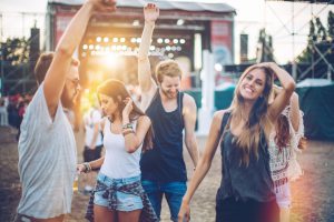 Young people having fun at concert. Stage in background. Summertime, evening. Caucasian ethnicity.